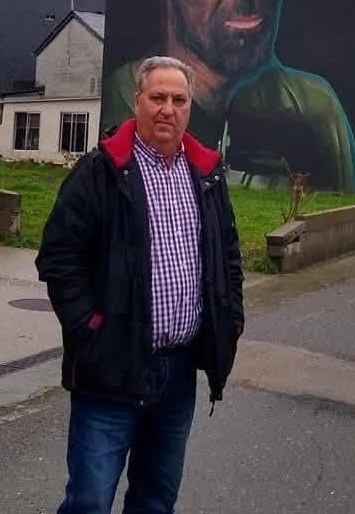 Rufino Gómez in a village street, in front of a mural of a miner